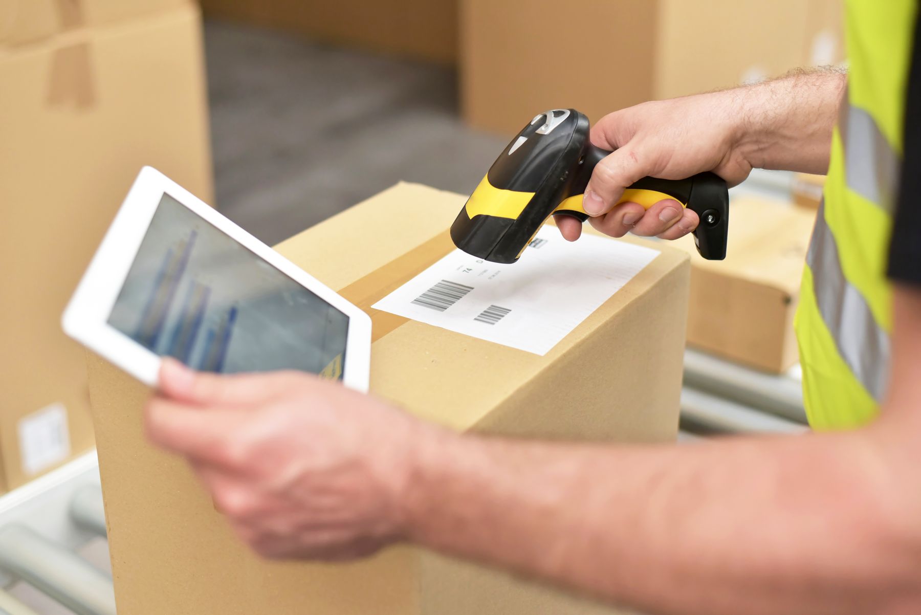 A warehouse worker scanning a carton barcode beside an operational tablet